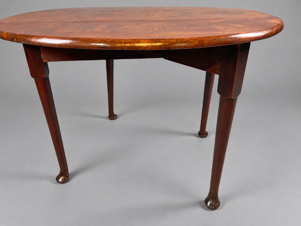 An 18th-century Georgian mahogany drop-leaf table featuring an oval top with rich grain figure and tapered legs ending in pad feet. View X