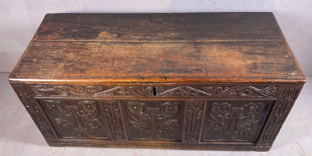 A 17th-century dark oak coffer featuring three relief-carved floral panels and a carved top frieze with a central keyhole.