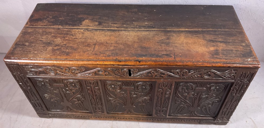 A 17th-century dark oak coffer featuring three relief-carved floral panels and a carved top frieze with a central keyhole. View II