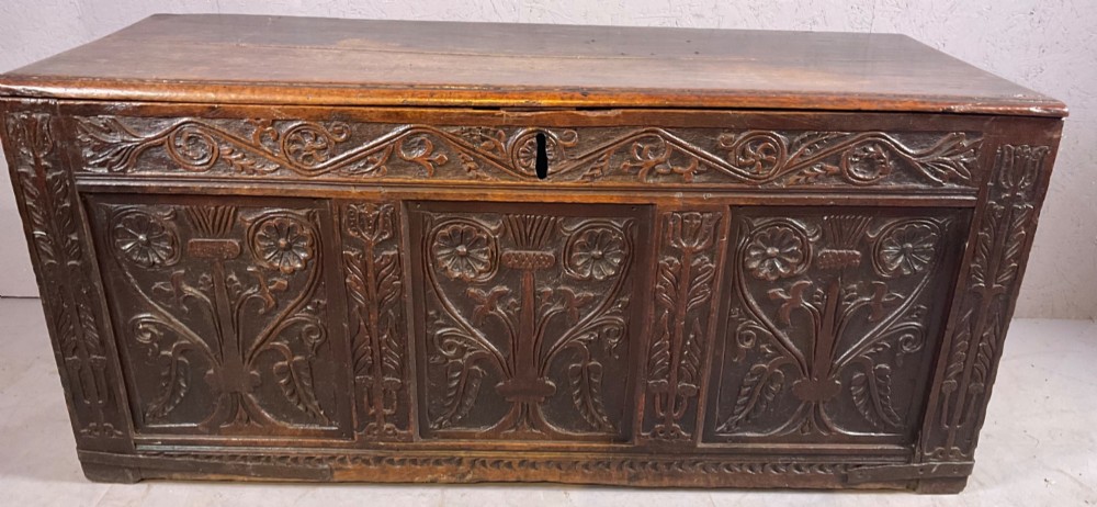 A 17th-century dark oak coffer featuring three relief-carved floral panels and a carved top frieze with a central keyhole. View III