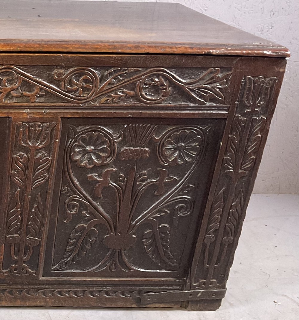 A 17th-century dark oak coffer featuring three relief-carved floral panels and a carved top frieze with a central keyhole. View V