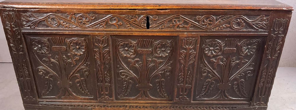 A 17th-century dark oak coffer featuring three relief-carved floral panels and a carved top frieze with a central keyhole. View VI
