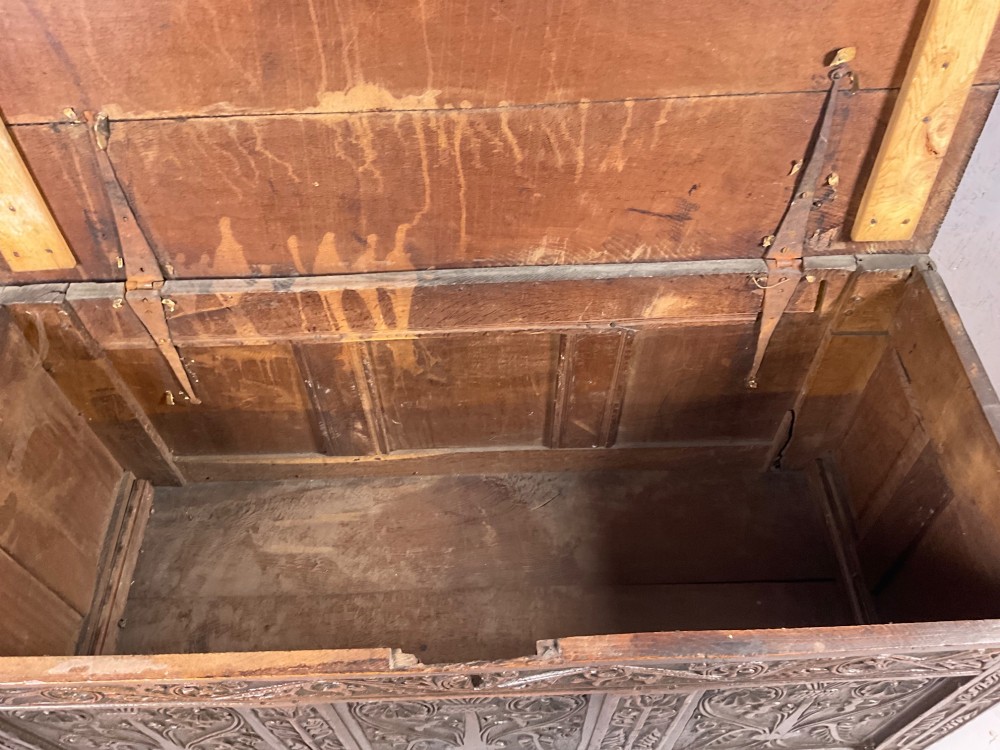 A 17th-century dark oak coffer featuring three relief-carved floral panels and a carved top frieze with a central keyhole. View X