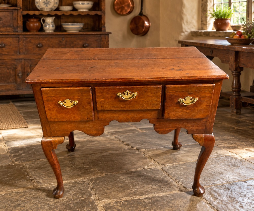 A Georgian oak lowboy featuring three drawers with brass handles, a shaped apron, and cabriole legs ending in pad feet. View V