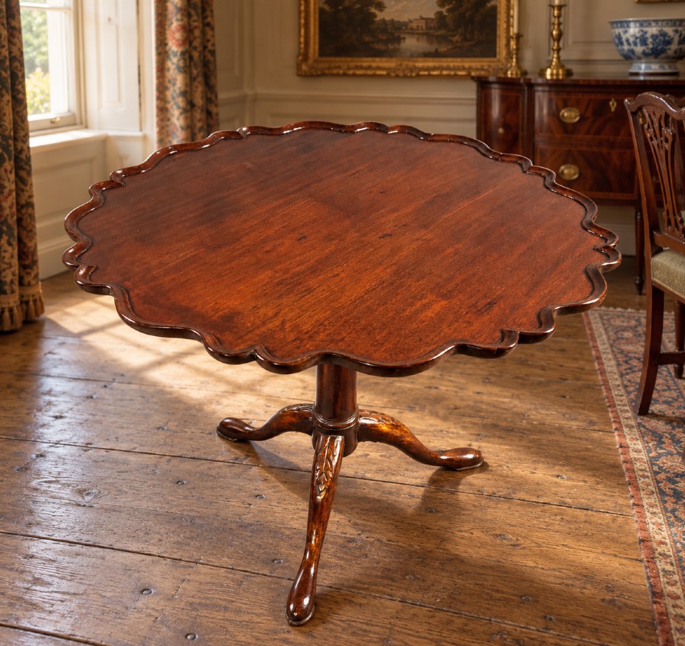 An 18th-century mahogany tilt-top supper table positioned vertically, displaying a scalloped piecrust edge rim and a turned tripod base with carved cabriole legs. View VIII