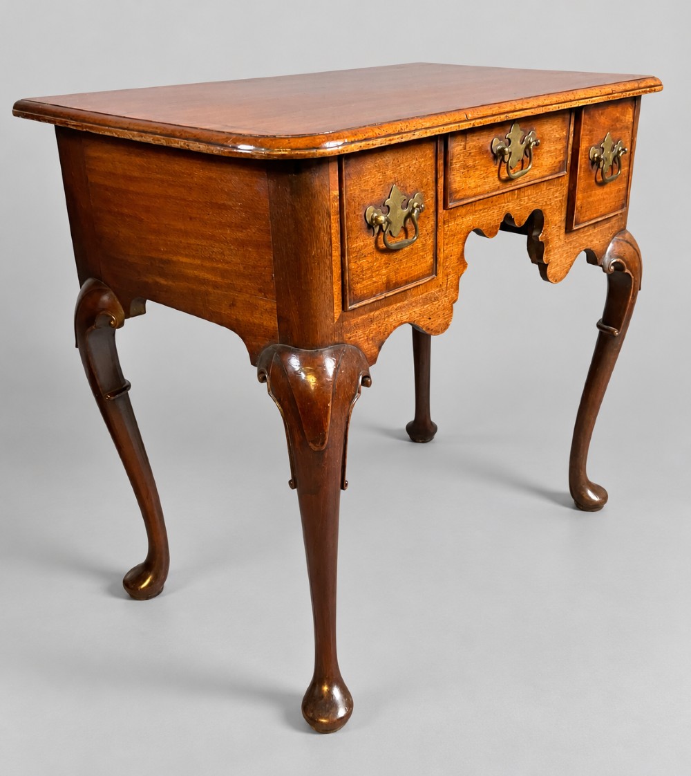 An 18th-century mahogany lowboy featuring three brass-handled drawers, a shaped apron, and four cabriole legs ending in pad feet.