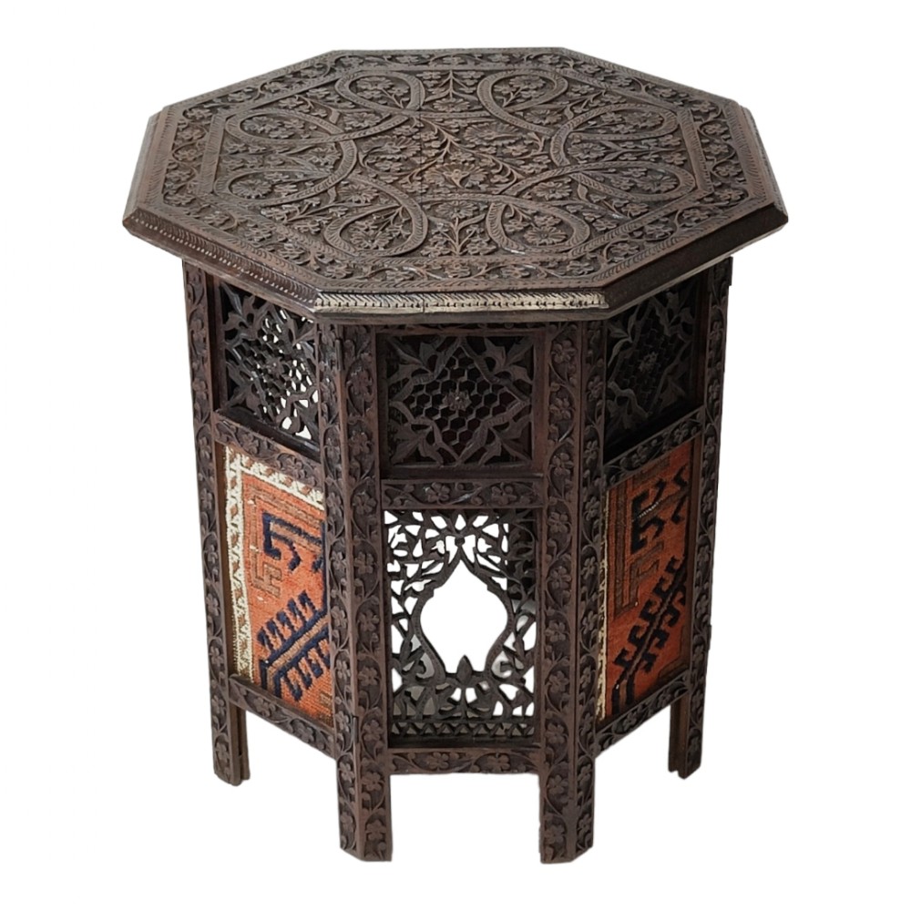 A dark brown hand-carved wooden octagonal occasional table with intricate foliate patterns, openwork panels, and woven textile insets.