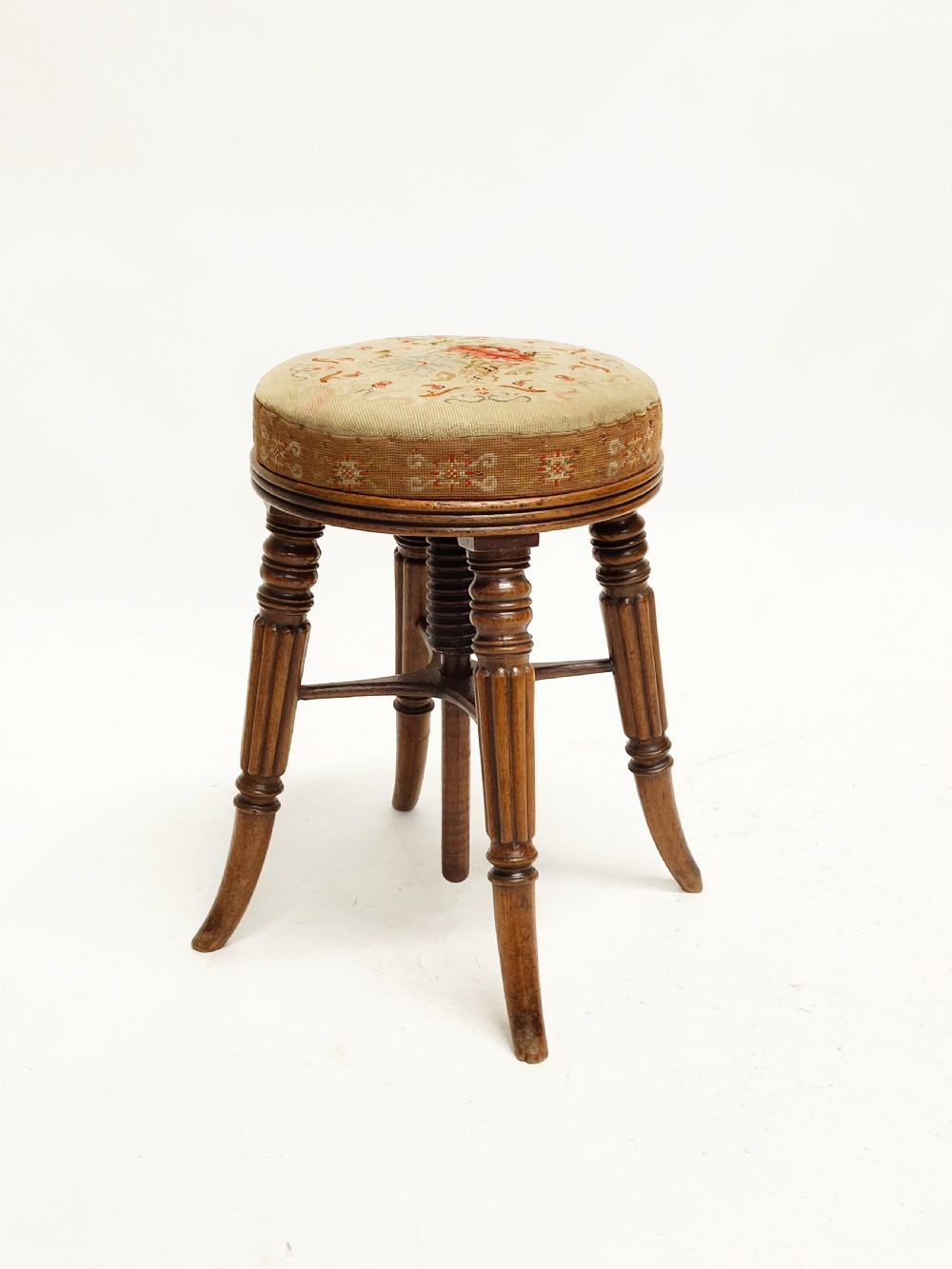 A Regency mahogany piano stool featuring a circular floral needlepoint upholstered seat, a wooden thread swivel mechanism, and four fluted legs.