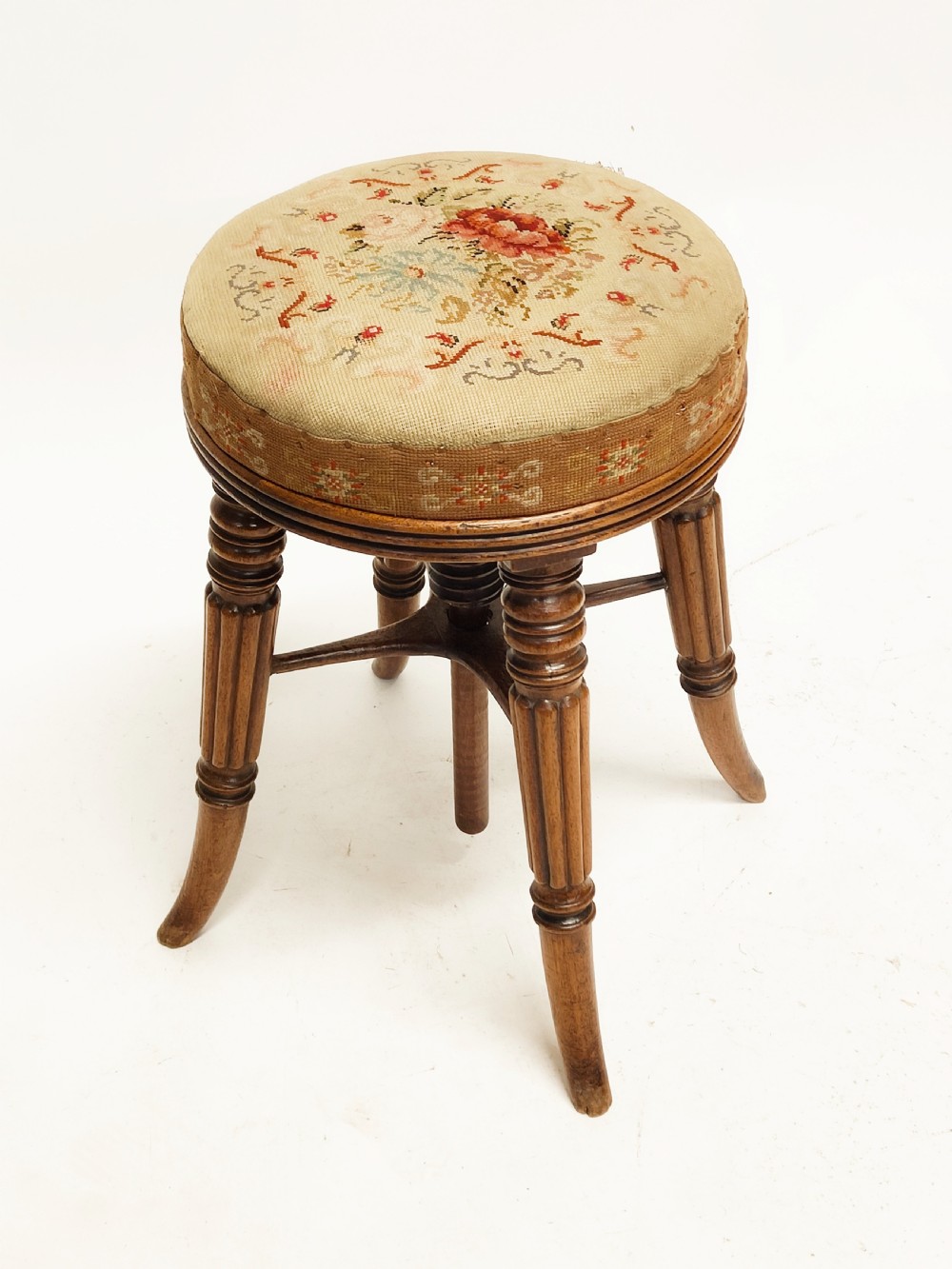 A Regency mahogany piano stool featuring a circular floral needlepoint upholstered seat, a wooden thread swivel mechanism, and four fluted legs. View IV
