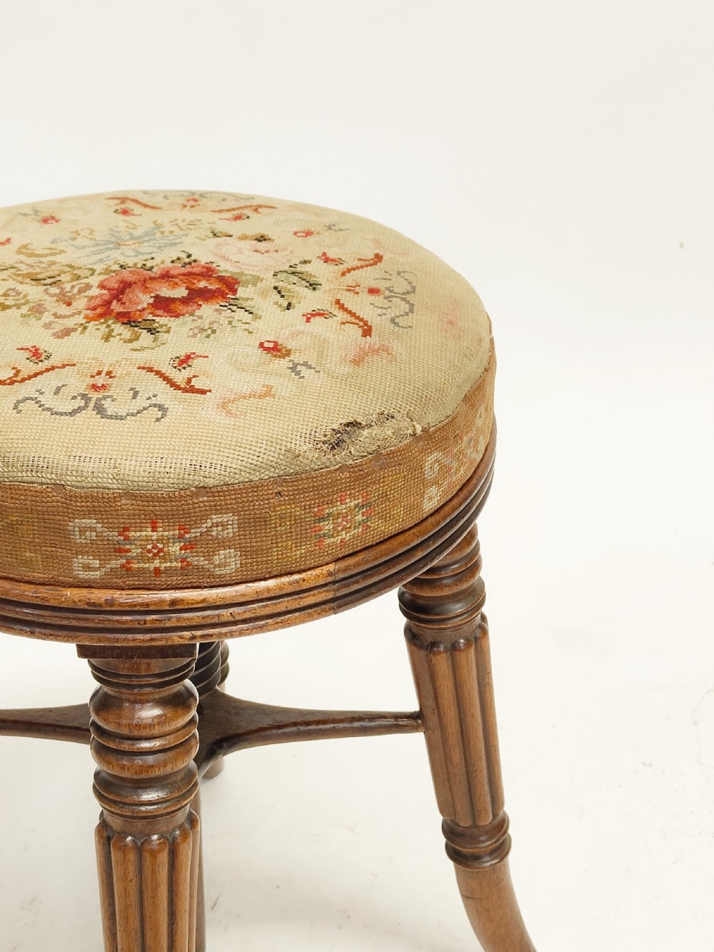 A Regency mahogany piano stool featuring a circular floral needlepoint upholstered seat, a wooden thread swivel mechanism, and four fluted legs. View V