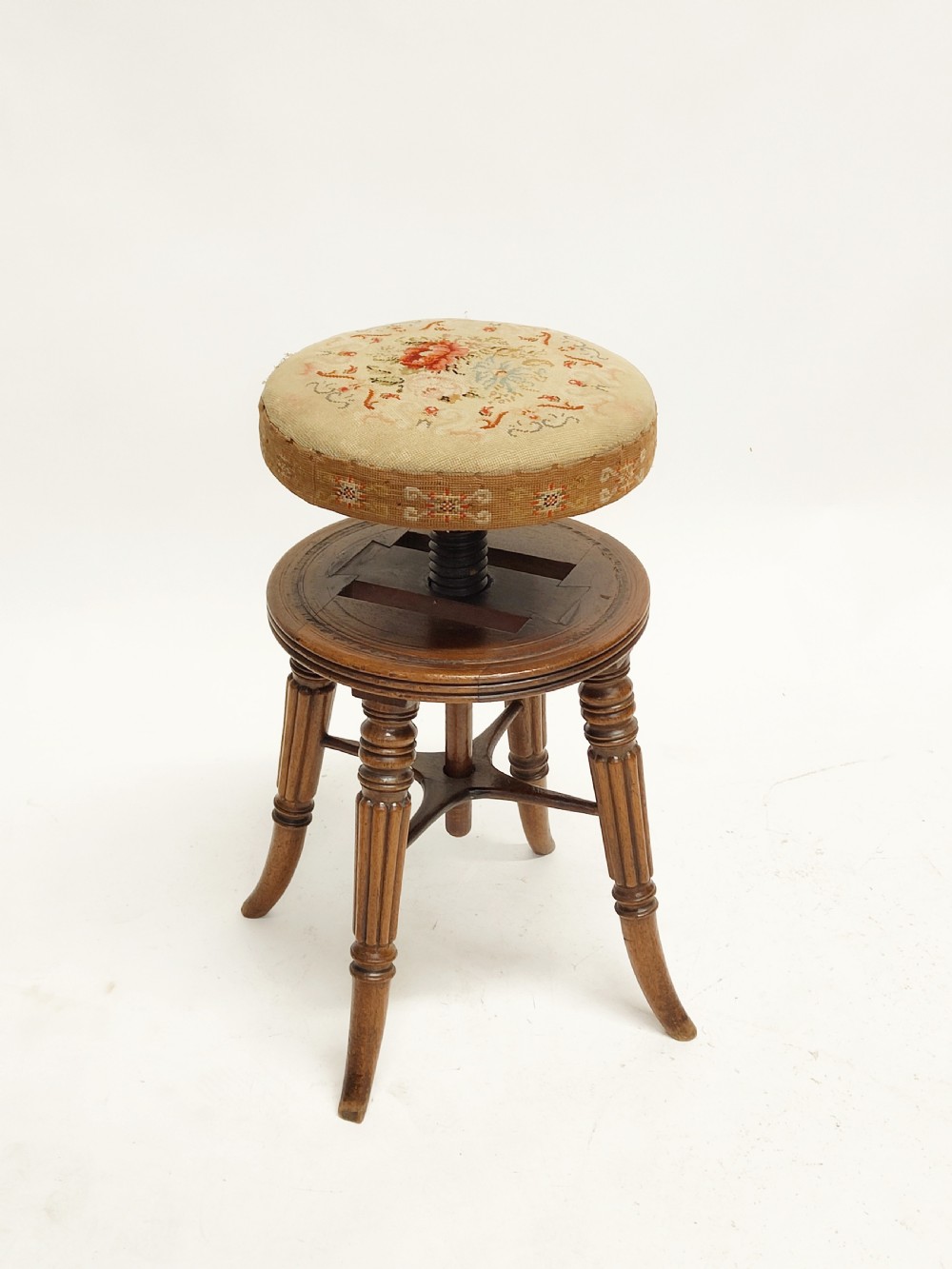 A Regency mahogany piano stool featuring a circular floral needlepoint upholstered seat, a wooden thread swivel mechanism, and four fluted legs. View VI