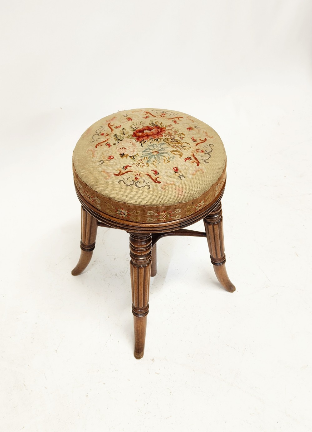 A Regency mahogany piano stool featuring a circular floral needlepoint upholstered seat, a wooden thread swivel mechanism, and four fluted legs. View VII