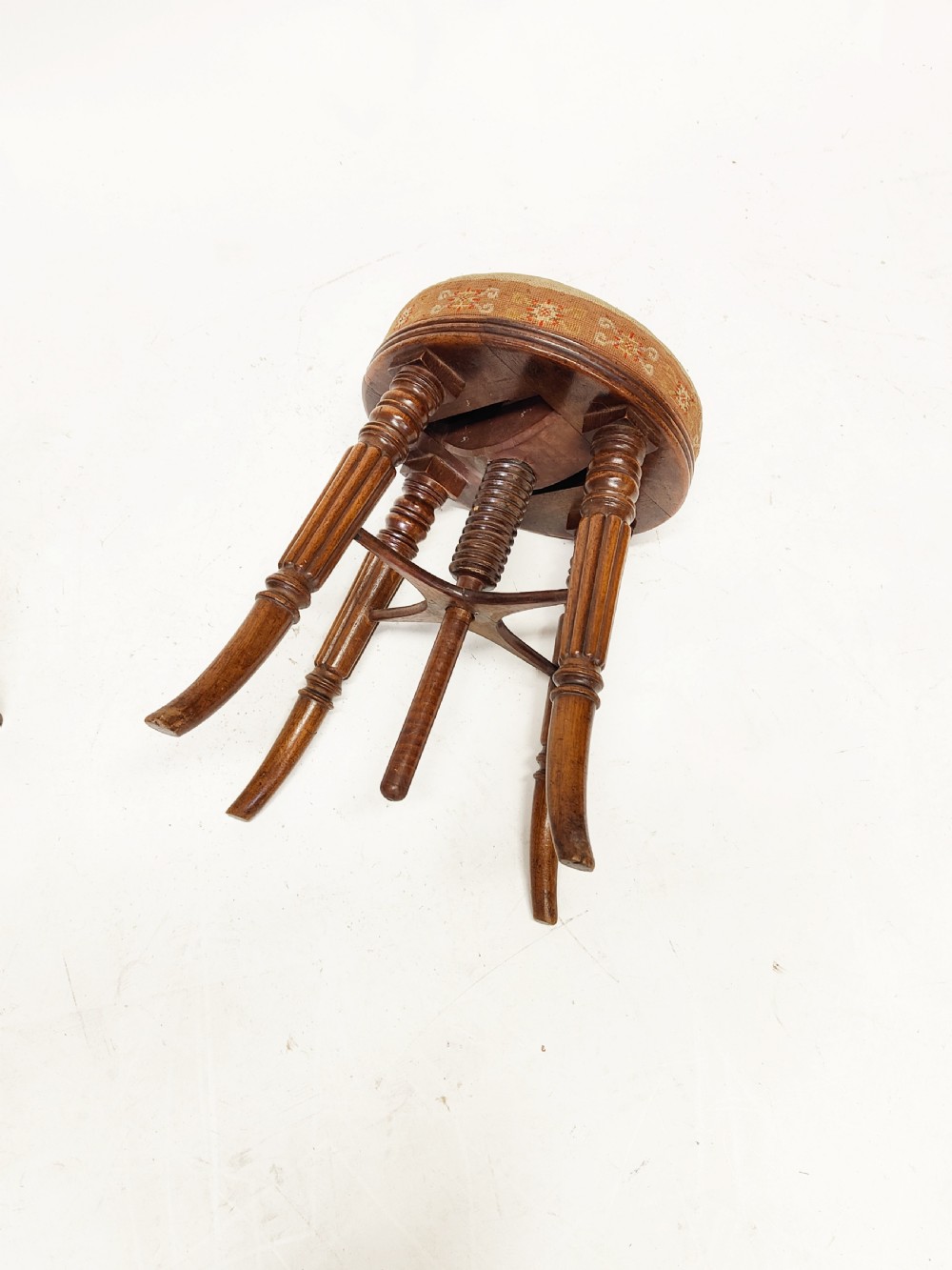 A Regency mahogany piano stool featuring a circular floral needlepoint upholstered seat, a wooden thread swivel mechanism, and four fluted legs. View IX