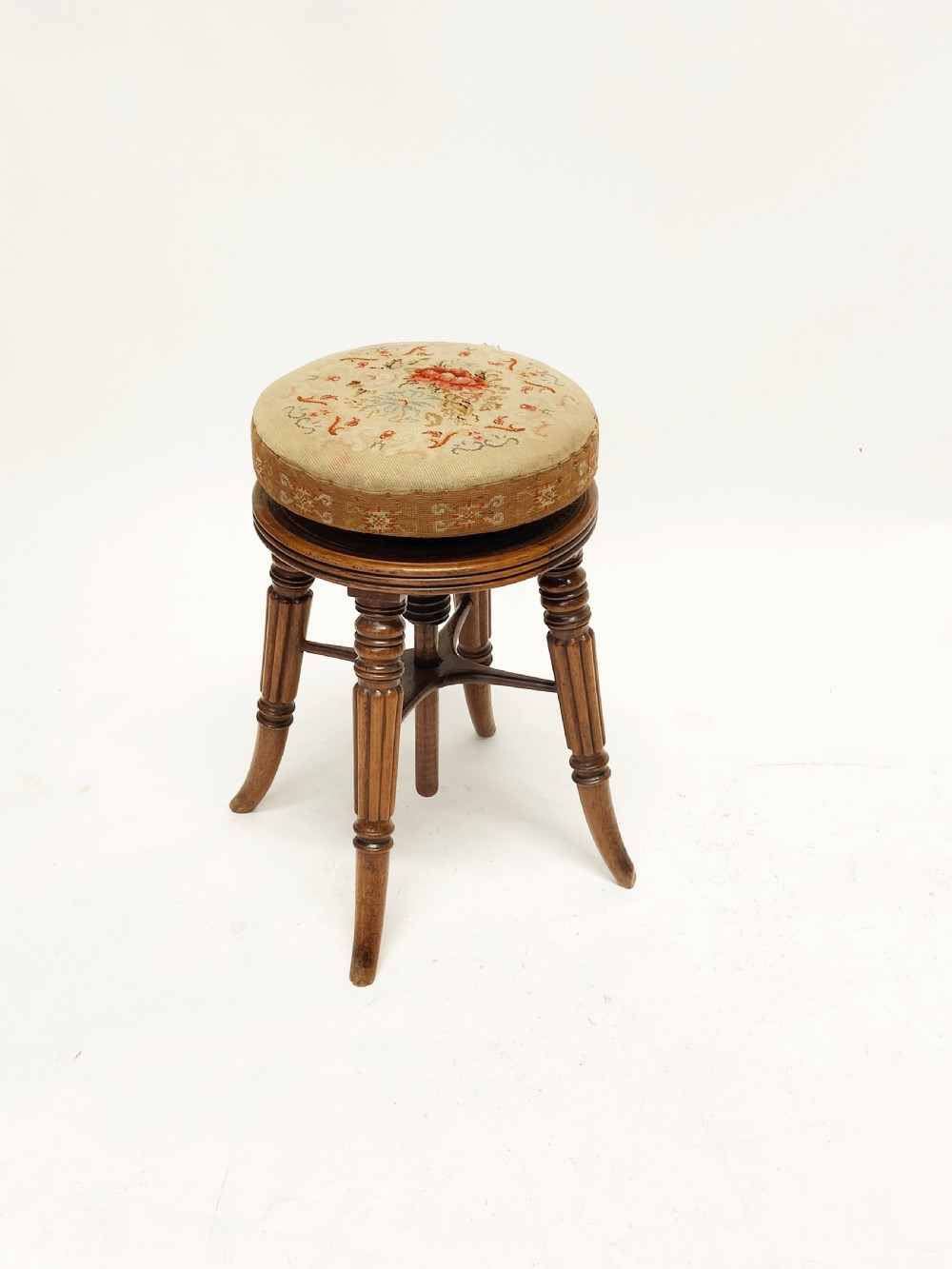 A Regency mahogany piano stool featuring a circular floral needlepoint upholstered seat, a wooden thread swivel mechanism, and four fluted legs. View X