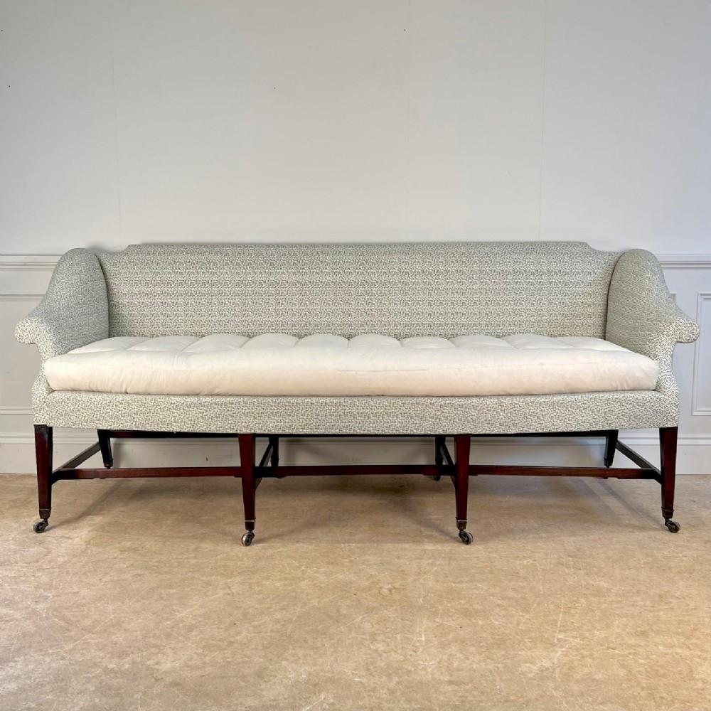 A George III upholstered sofa featuring a patterned sage green fabric, a long cushioned seat, and six dark mahogany legs with brass castors.