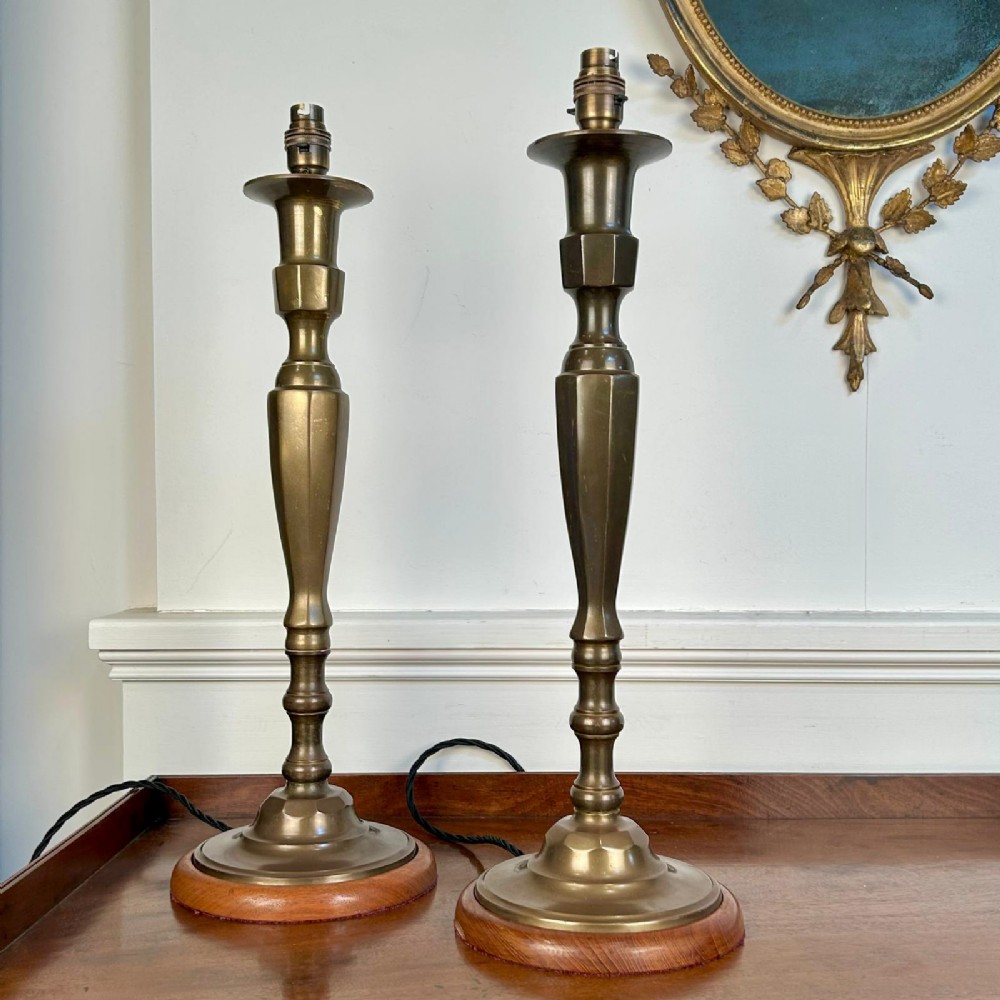 A pair of Edwardian brass candlestick-style table lamps with faceted columns set upon circular wooden bases.