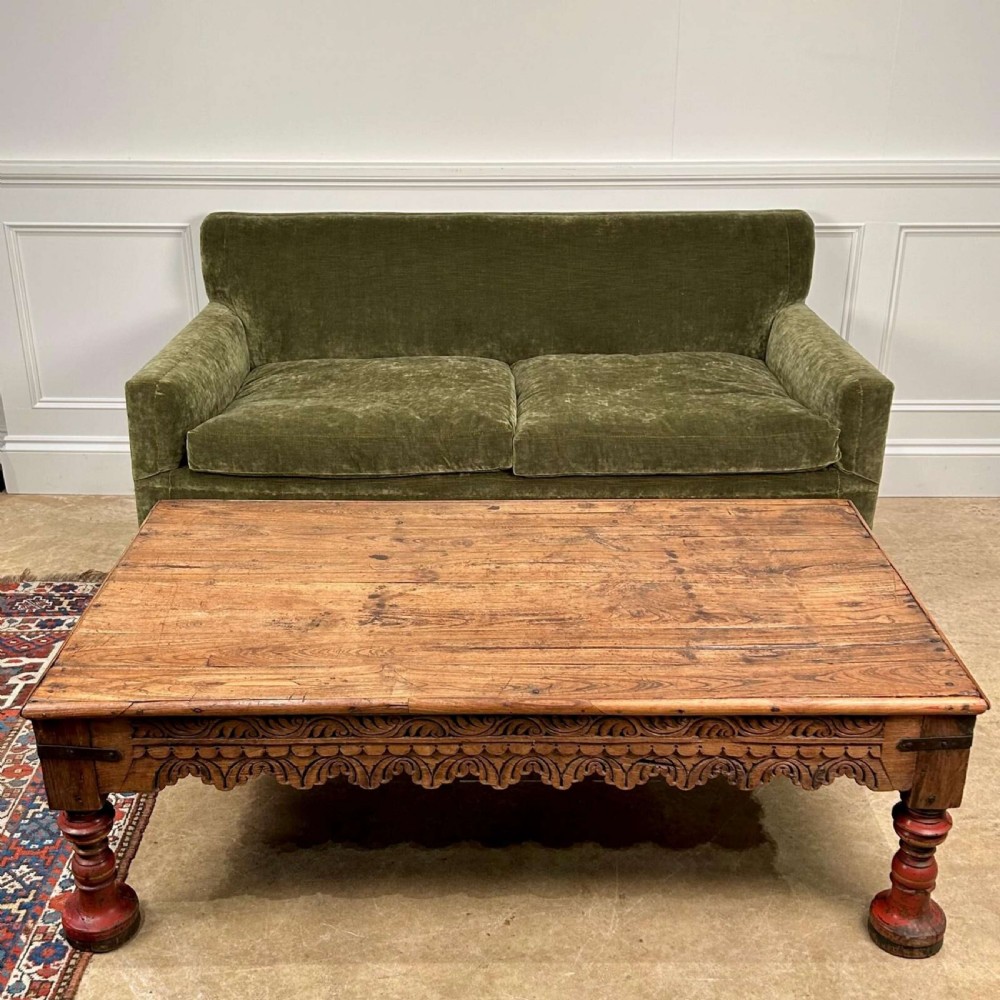 A low 19th-century Indian Takhat coffee table crafted from warm brown timber featuring a carved scalloped apron, iron corner brackets, and red turned legs. View V