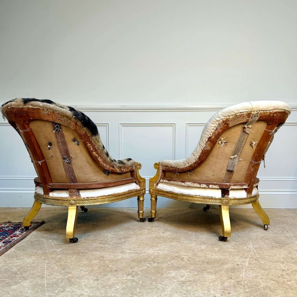 A pair of 19th-century Victorian giltwood armchairs with carved fluted legs, brass castors, and button-backed calico upholstery prepared for restoration. View II