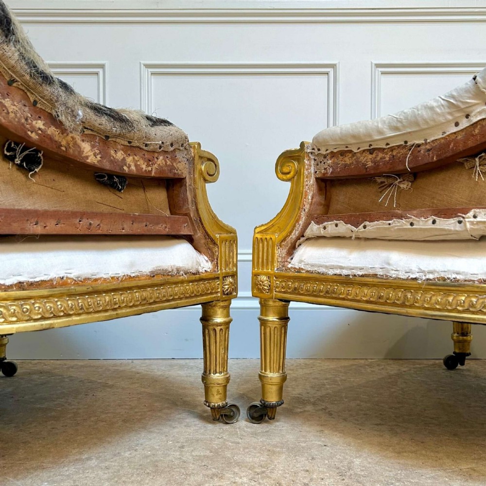A pair of 19th-century Victorian giltwood armchairs with carved fluted legs, brass castors, and button-backed calico upholstery prepared for restoration. View III