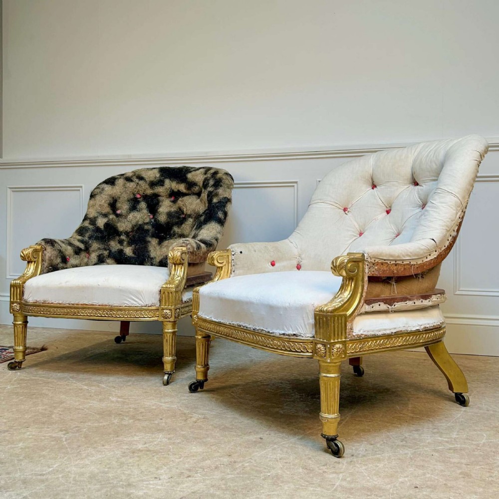 A pair of 19th-century Victorian giltwood armchairs with carved fluted legs, brass castors, and button-backed calico upholstery prepared for restoration. View IV