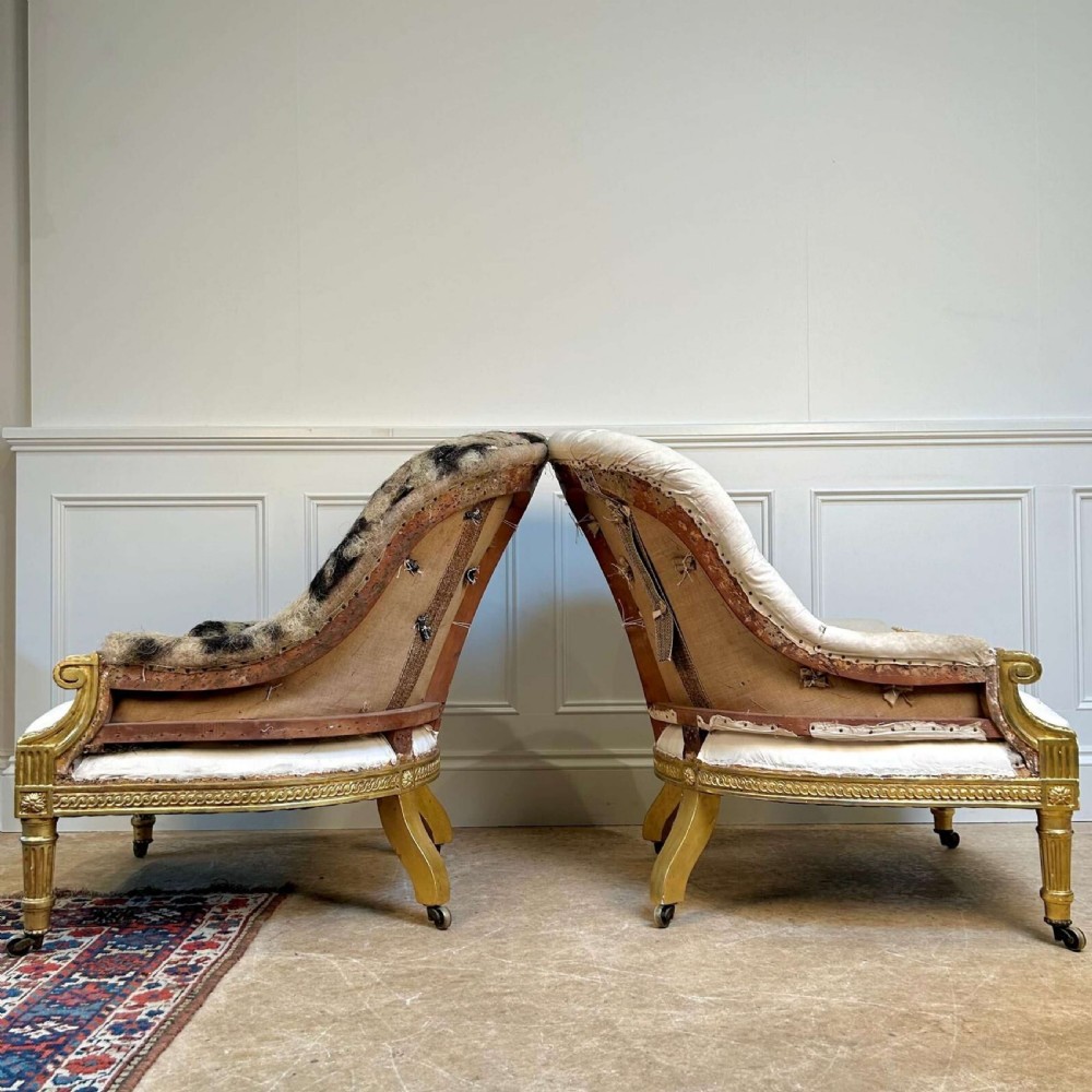 A pair of 19th-century Victorian giltwood armchairs with carved fluted legs, brass castors, and button-backed calico upholstery prepared for restoration. View V