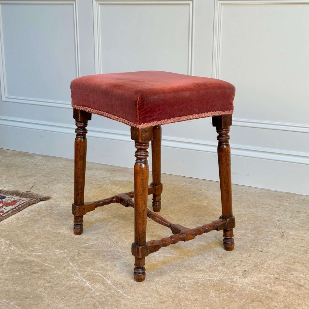 A Georgian mahogany stool featuring turned legs and stretchers beneath a rose velvet square upholstered seat with braided trim. View II