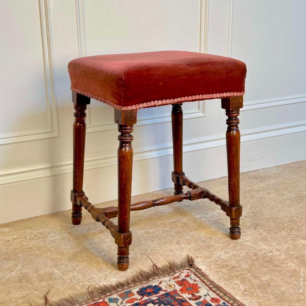 A Georgian mahogany stool featuring turned legs and stretchers beneath a rose velvet square upholstered seat with braided trim. View IV