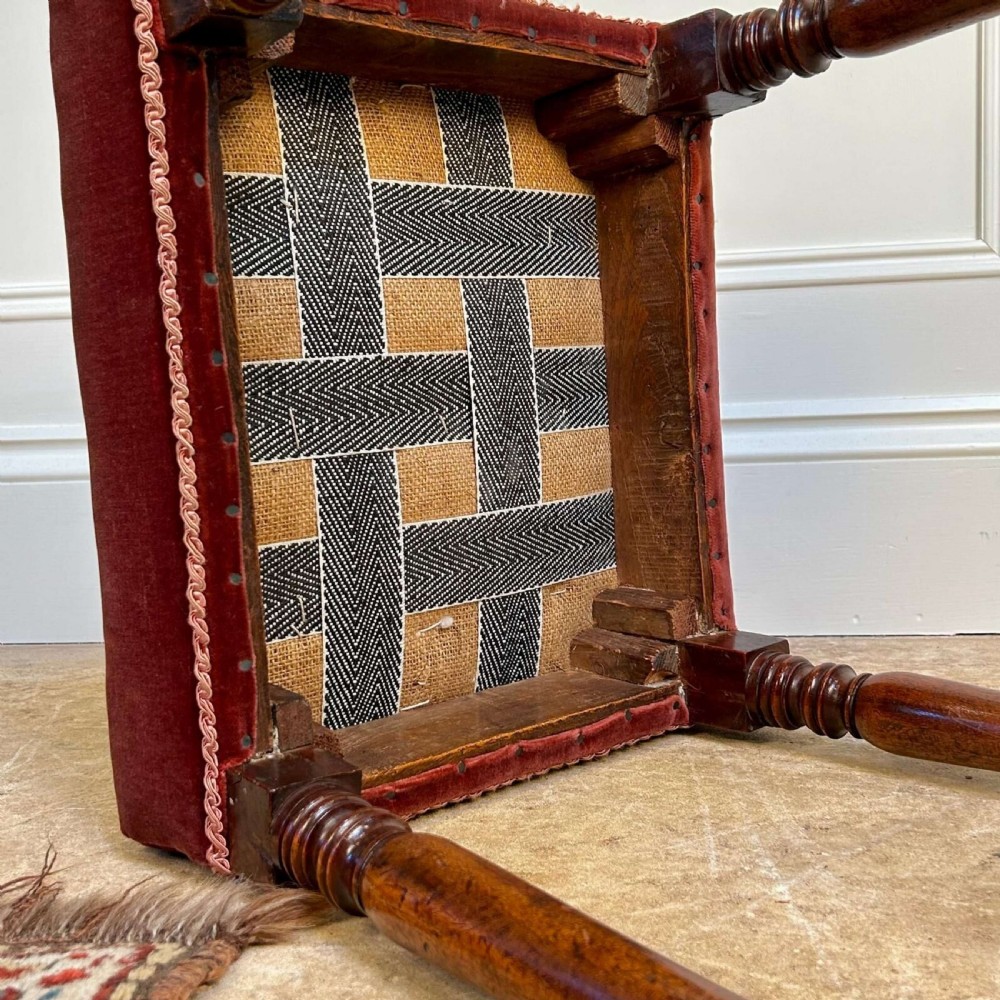 A Georgian mahogany stool featuring turned legs and stretchers beneath a rose velvet square upholstered seat with braided trim. View V