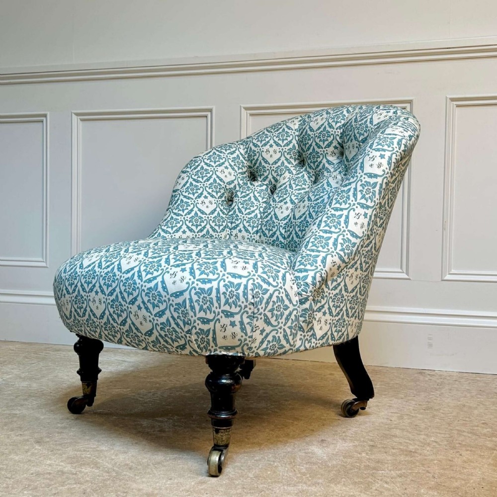 A low 19th-century armless slipper chair with blue and white botanical patterned upholstery, deep buttoned backrest, turned front legs, and brass castors.