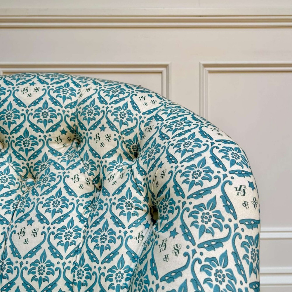 A low 19th-century armless slipper chair with blue and white botanical patterned upholstery, deep buttoned backrest, turned front legs, and brass castors. View III