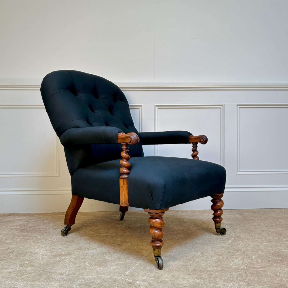 A 19th-century Victorian open armchair featuring black button-tufted fabric upholstery, barley twist wooden arm supports and front legs, and brass castors.