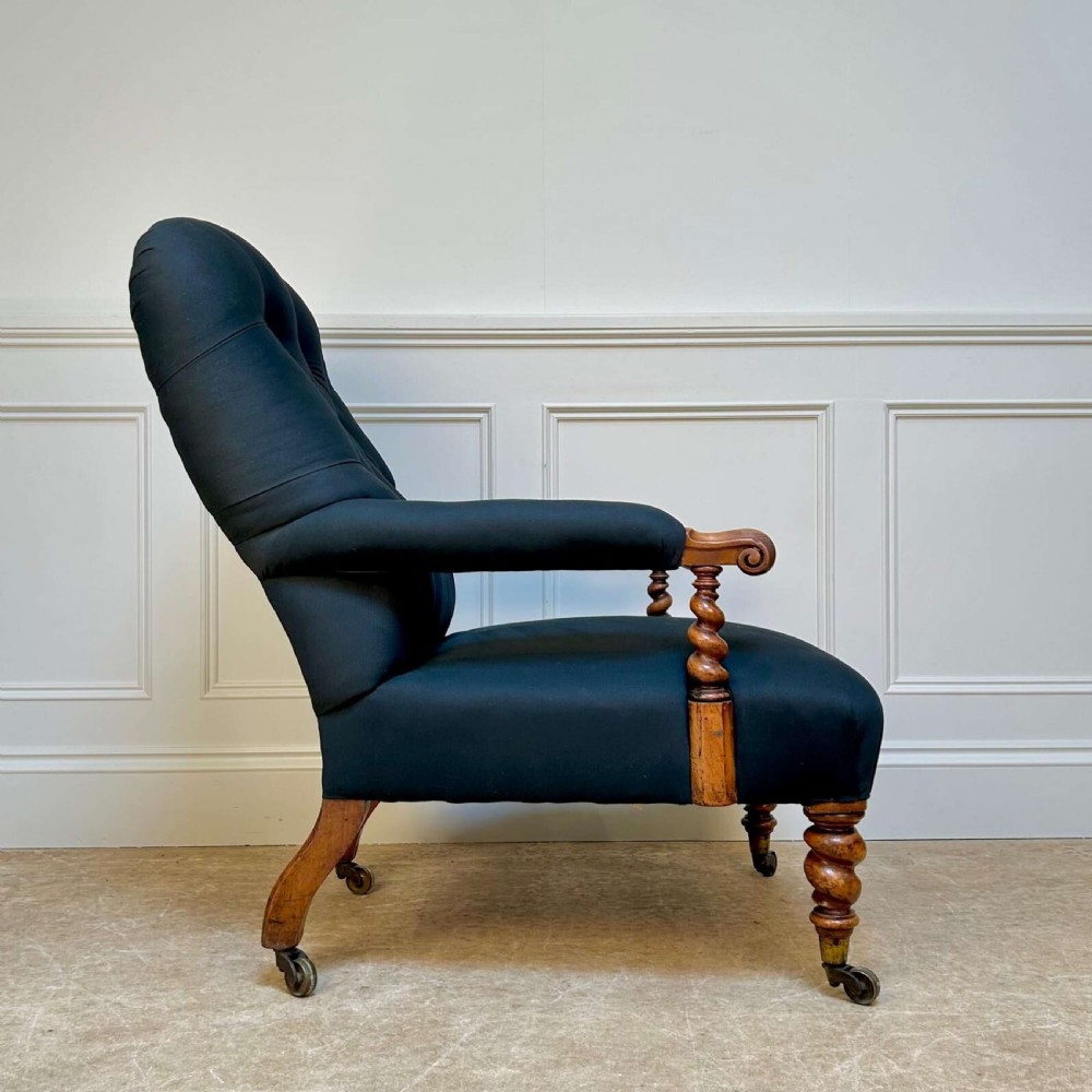 A 19th-century Victorian open armchair featuring black button-tufted fabric upholstery, barley twist wooden arm supports and front legs, and brass castors. View III