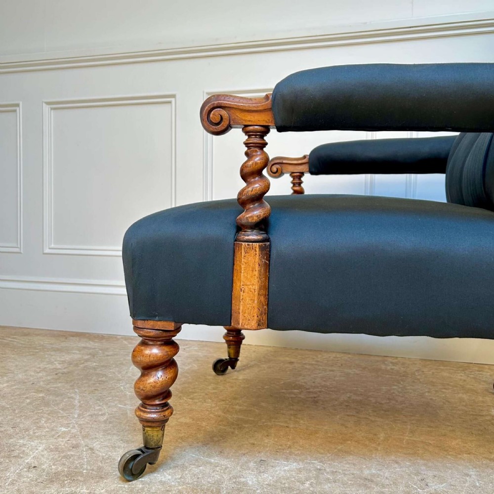 A 19th-century Victorian open armchair featuring black button-tufted fabric upholstery, barley twist wooden arm supports and front legs, and brass castors. View IV