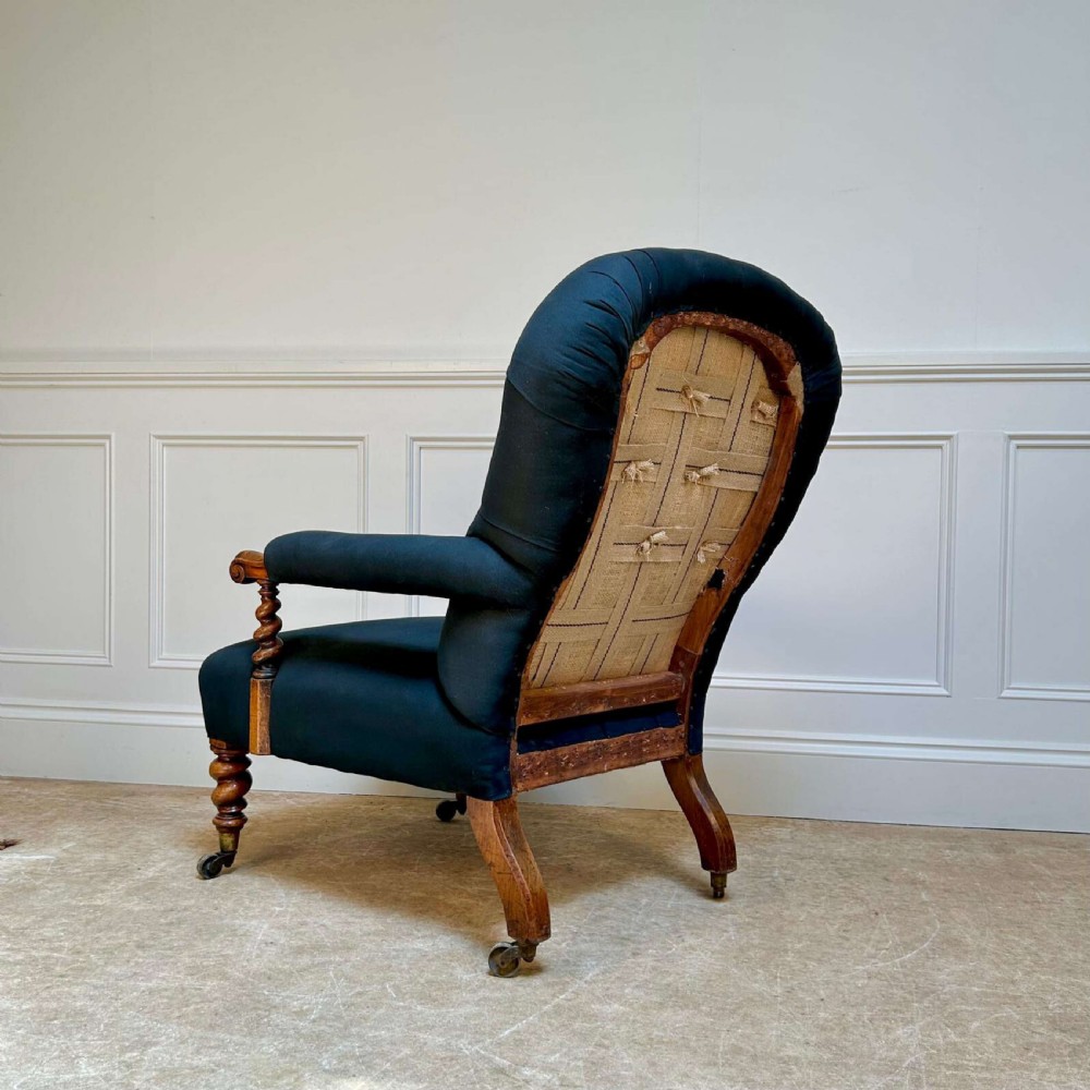 A 19th-century Victorian open armchair featuring black button-tufted fabric upholstery, barley twist wooden arm supports and front legs, and brass castors. View V