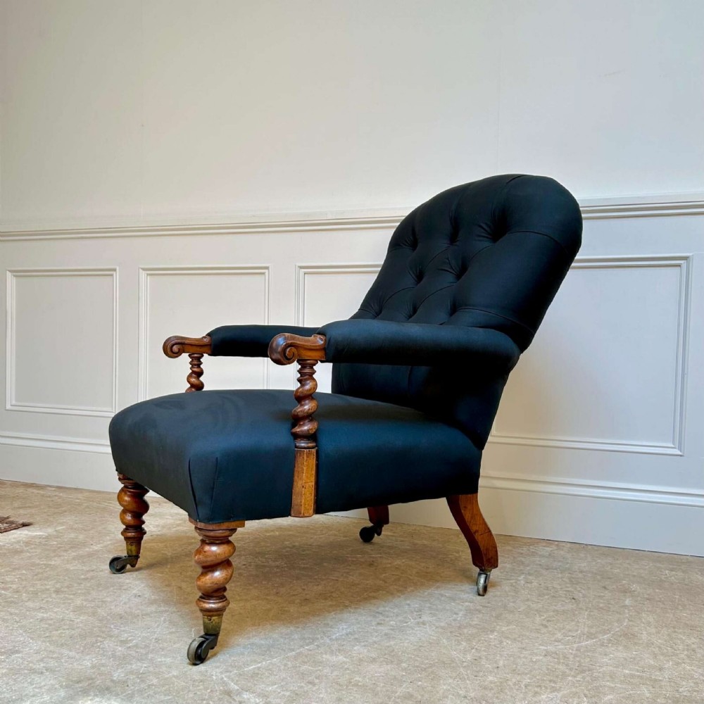 A 19th-century Victorian open armchair featuring black button-tufted fabric upholstery, barley twist wooden arm supports and front legs, and brass castors. View VI