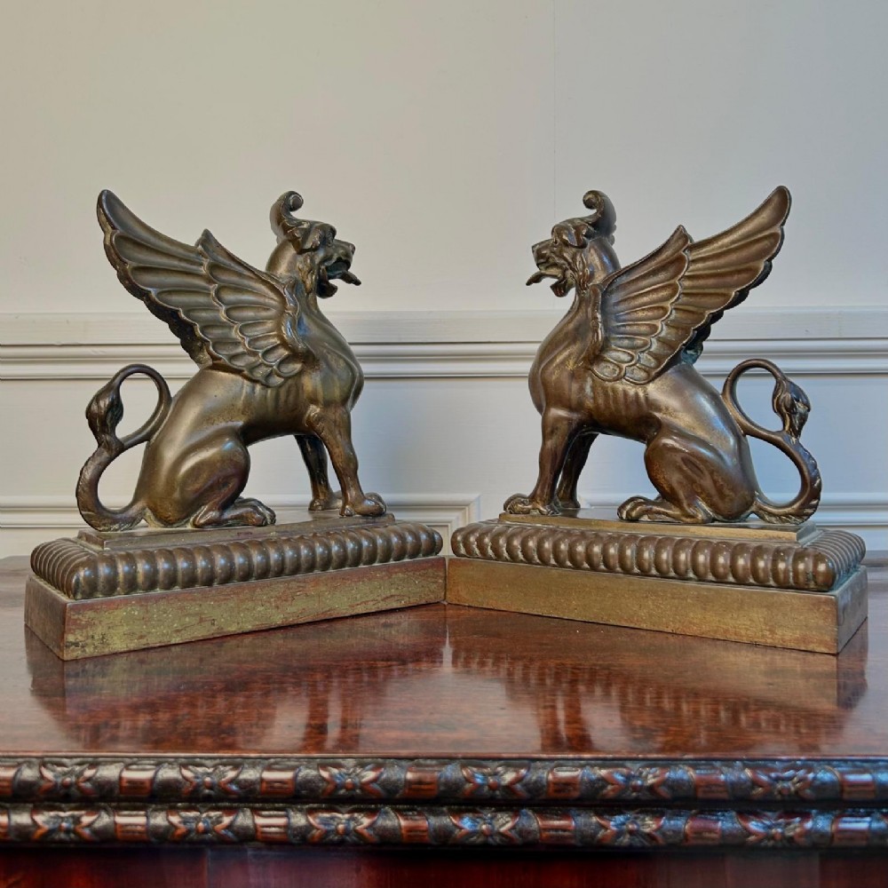 A pair of 19th-century bronzed metal griffin sculptures facing each other, mounted on stepped rectangular bases.