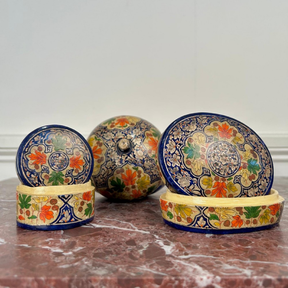 A set of three circular hand-painted Kashmiri papier-mache lidded pots adorned with intricate blue, gold, and foliage patterns.