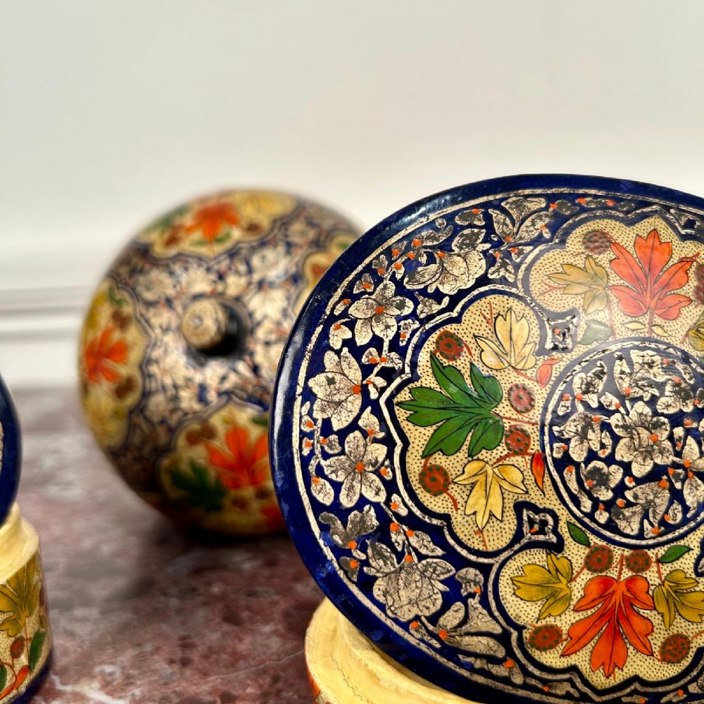 A set of three circular hand-painted Kashmiri papier-mache lidded pots adorned with intricate blue, gold, and foliage patterns. View II