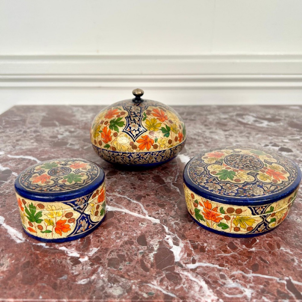 A set of three circular hand-painted Kashmiri papier-mache lidded pots adorned with intricate blue, gold, and foliage patterns. View III