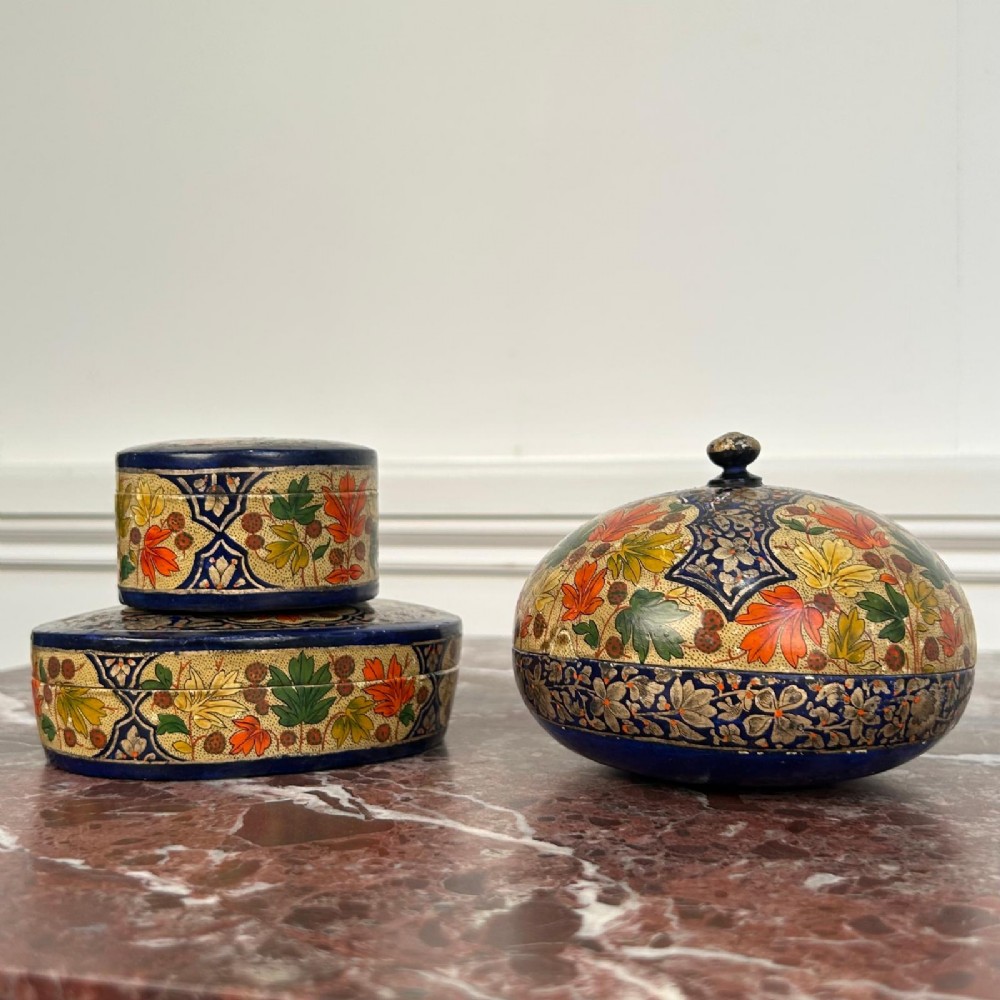 A set of three circular hand-painted Kashmiri papier-mache lidded pots adorned with intricate blue, gold, and foliage patterns. View V
