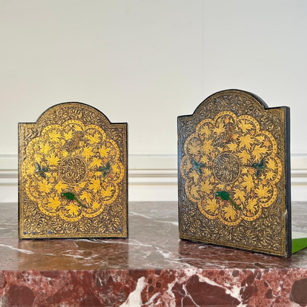 A pair of arched Kashmiri bookends decorated with intricate gold floral patterns, chinar leaves, and colourful painted birds on a dark background.