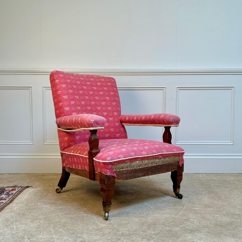 A nineteenth-century Arts and Crafts armchair featuring pink floral fabric upholstery, turned mahogany front legs, and brass castors.