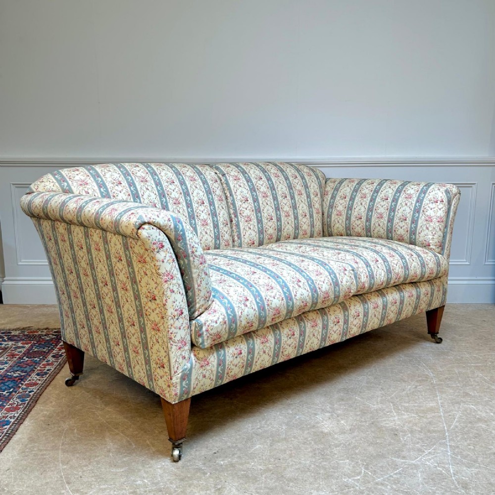 A two-seater Howard & Sons Chaplin sofa upholstered in cream, blue-striped, and floral patterned fabric with tapered wooden legs on brass castors. View II