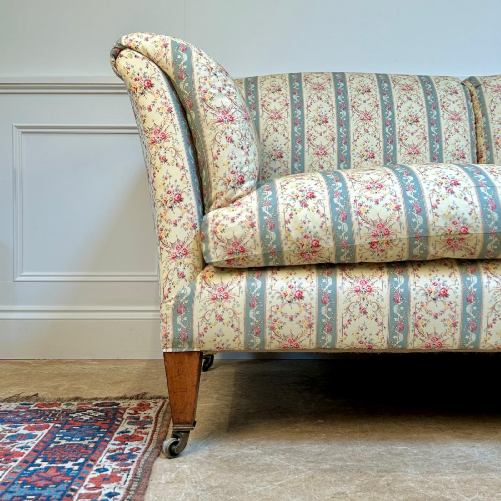 A two-seater Howard & Sons Chaplin sofa upholstered in cream, blue-striped, and floral patterned fabric with tapered wooden legs on brass castors. View VI