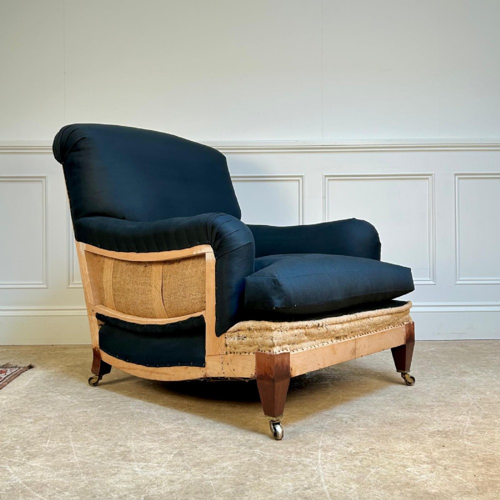 A 1930s Bridgewater style armchair upholstered in dark fabric with an exposed timber lower frame, hessian lining, and mahogany legs with brass castors.