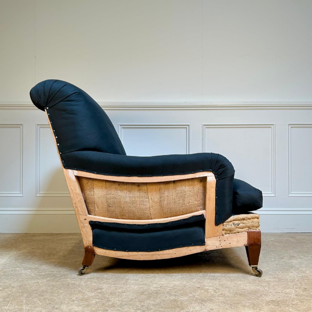 A 1930s Bridgewater style armchair upholstered in dark fabric with an exposed timber lower frame, hessian lining, and mahogany legs with brass castors. View II