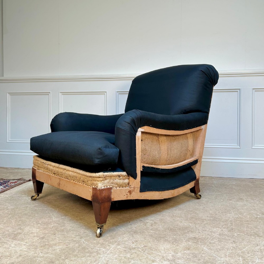 A 1930s Bridgewater style armchair upholstered in dark fabric with an exposed timber lower frame, hessian lining, and mahogany legs with brass castors. View III