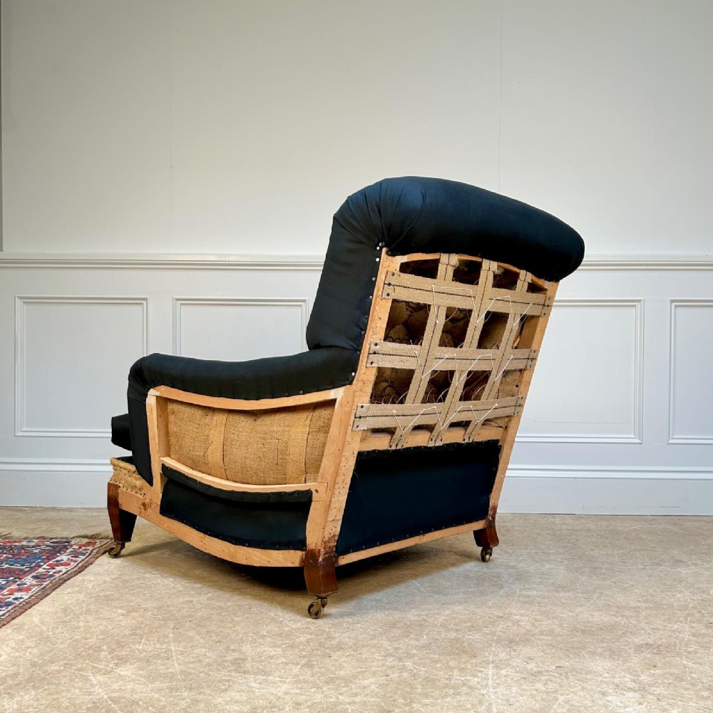 A 1930s Bridgewater style armchair upholstered in dark fabric with an exposed timber lower frame, hessian lining, and mahogany legs with brass castors. View IV