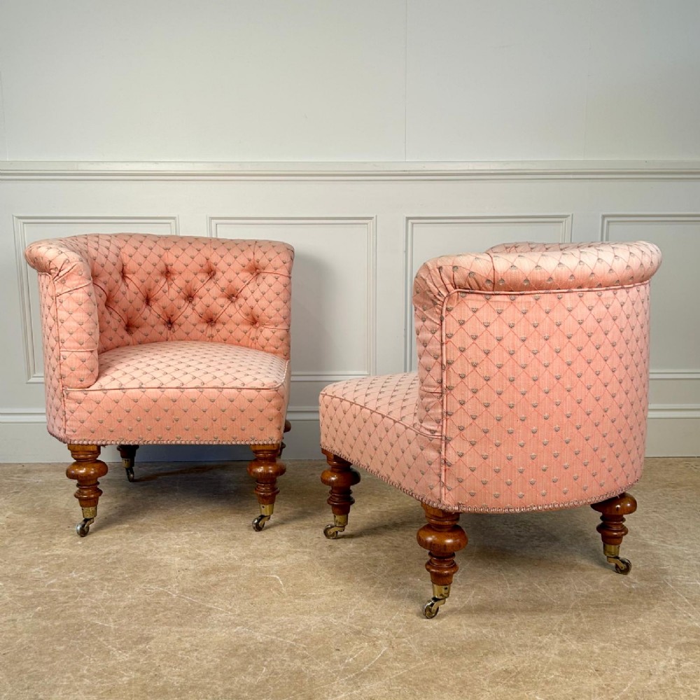 A pair of 19th-century corner armchairs upholstered in pink diamond-patterned fabric featuring button-tufted rounded backs and turned oak legs on brass castors.