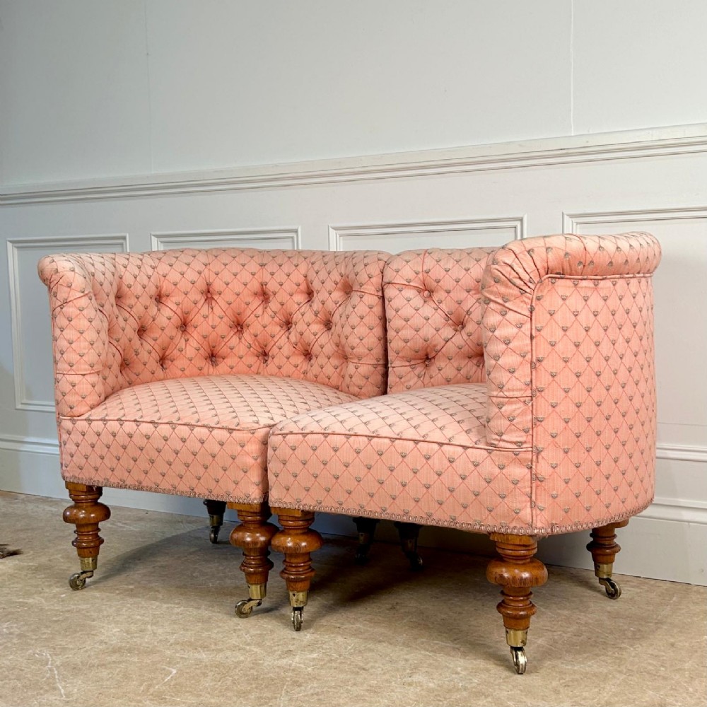A pair of 19th-century corner armchairs upholstered in pink diamond-patterned fabric featuring button-tufted rounded backs and turned oak legs on brass castors. View V